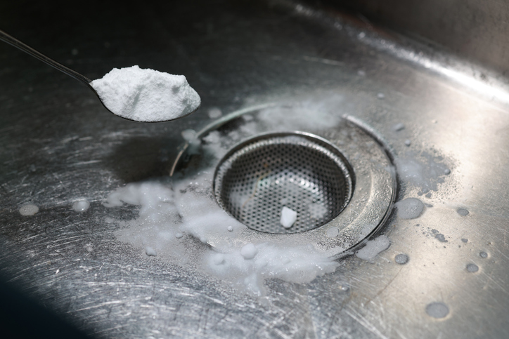 kitchen sink drain. a spoon with baking soda is being poured into a clogged drain