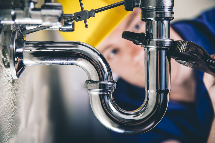 A plumber is fixing a set of pipes under a sink. Protecting Your Pipes During the Winter.