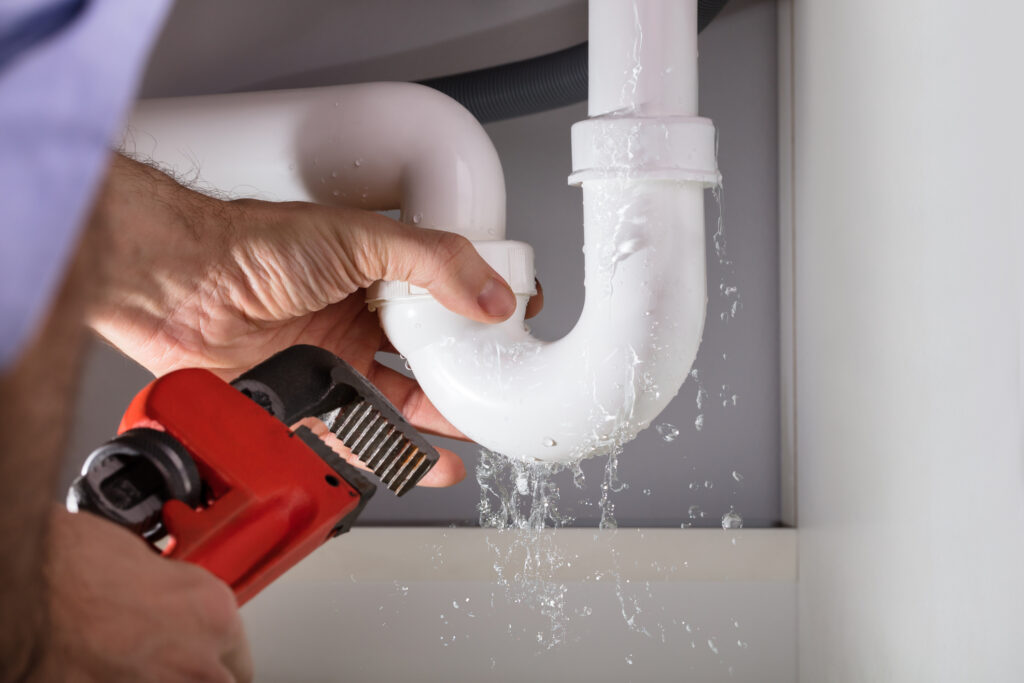 Close-up Of Male Neighborhood Plumber Fixing White Sink Pipe With Adjustable Wrench