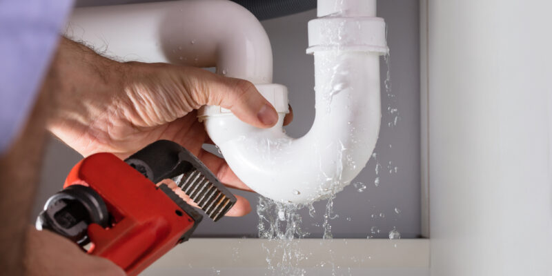 Close-up Of Male Neighborhood Plumber Fixing White Sink Pipe With Adjustable Wrench